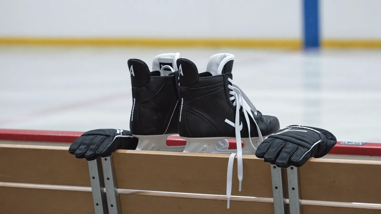 Black hockey skates and gloves resting on a wooden bench beside the ice