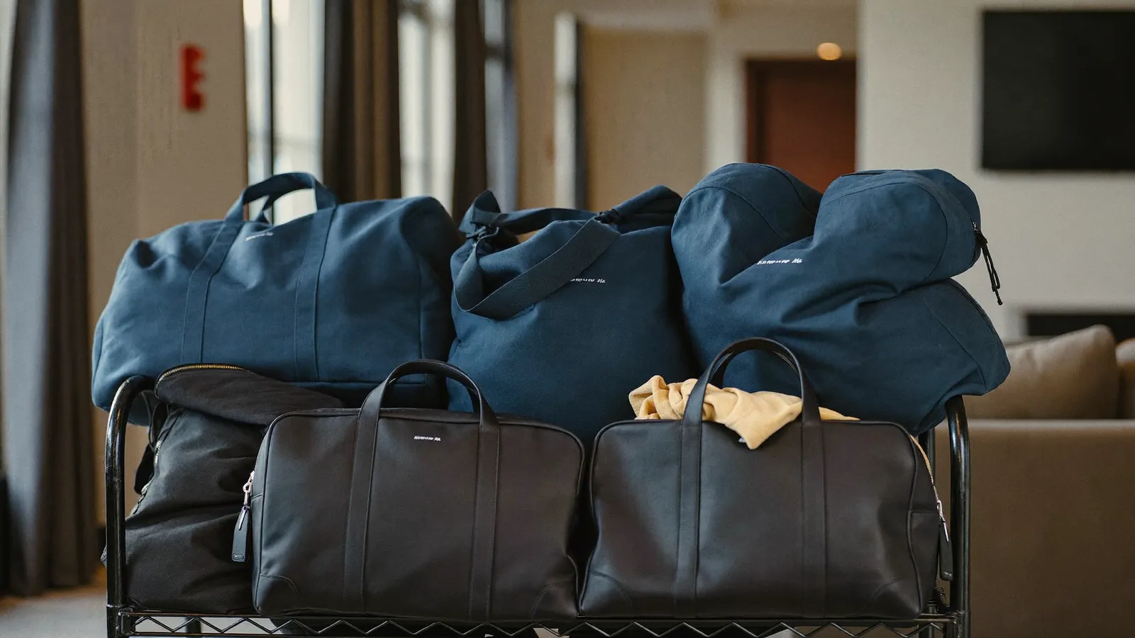 Navy and black duffel bags piled on a luggage cart in a bright hotel lobby