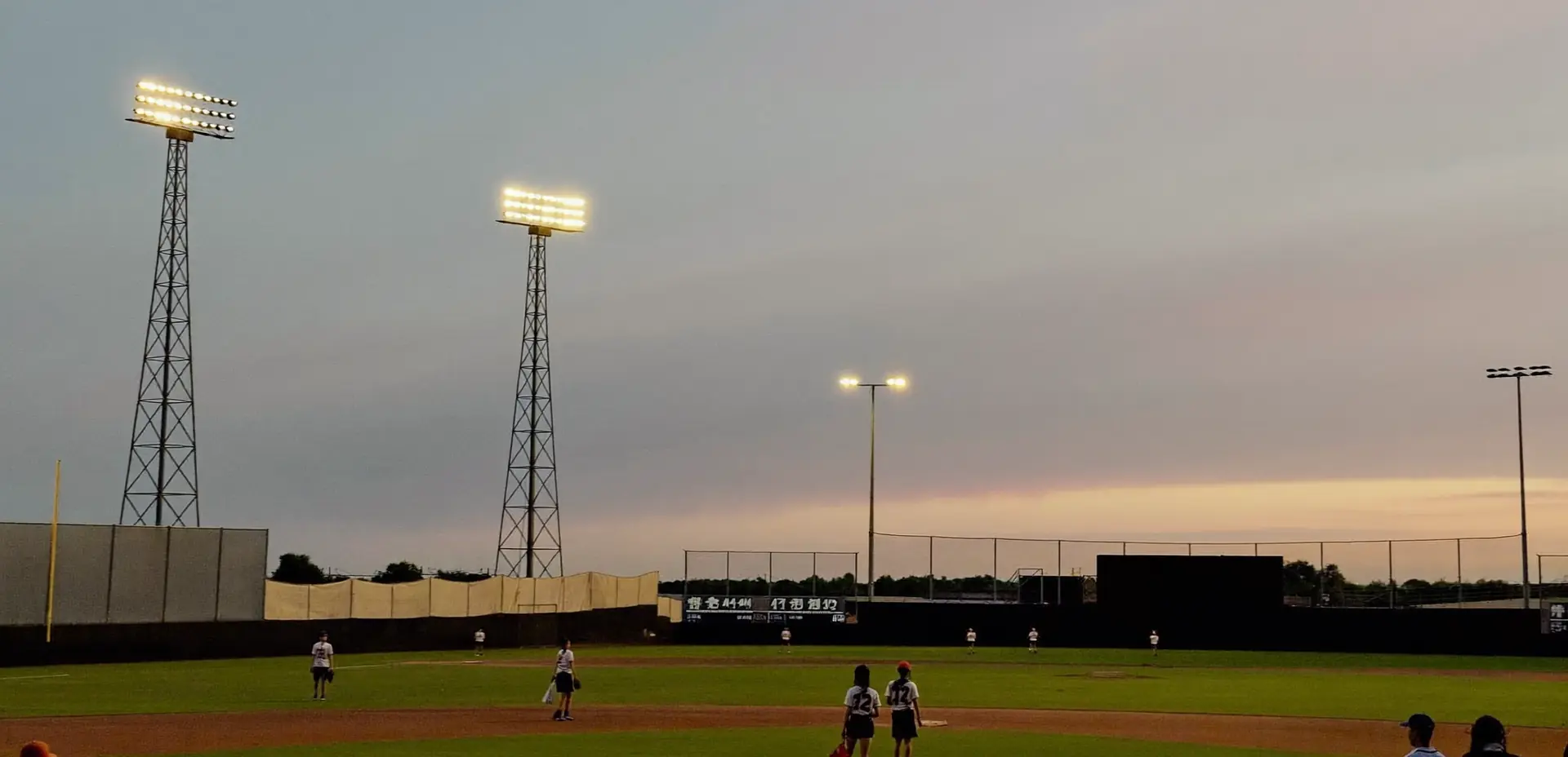 Youth baseball tournament complex at dusk under stadium lights