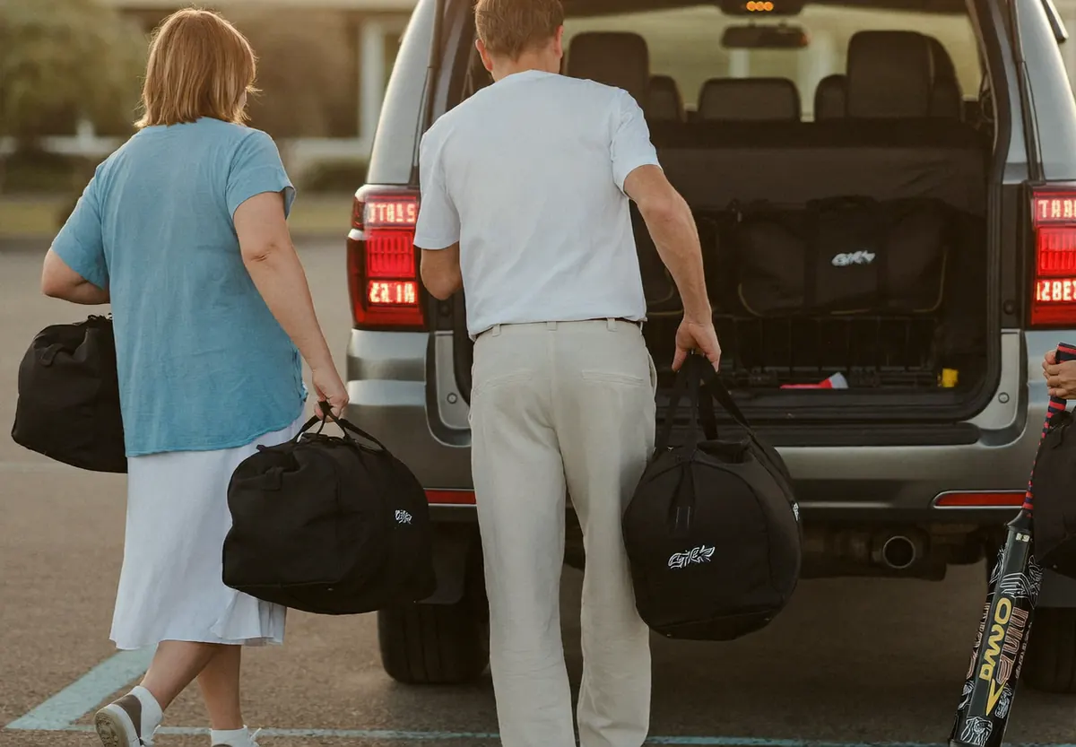 Parents loading duffel bags into an SUV in a hotel parking lot